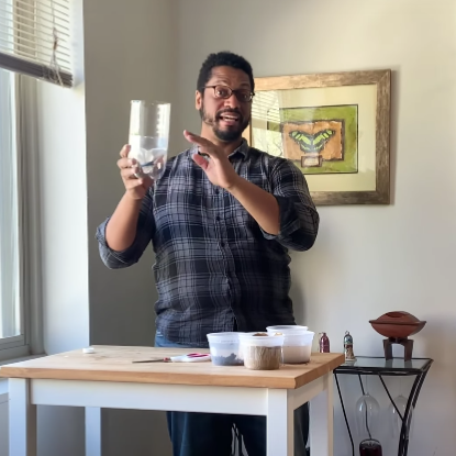 AJ stands behind a table, holding a clear plastic jug and smiling.
