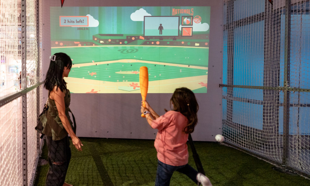 Young girl swinging a bat at the virtual Grand Slam Science experience in the Engineering Games + Play exhibit